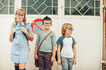 Group of three funny kids wearing backpacks walking back to school. Girl and boys wearing...