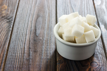 Fototapeta na wymiar White sugar in bowl on wooden background. Selective focus, horizontal. Intake of bad calories.