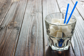 Glass with straw full of sugar and sugar cubes on wooden background