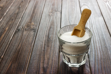 White granulated sugar in white cup with wooden spoon on wooden background.