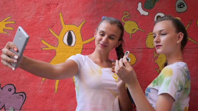 Selphi of girls with spinners in arms on background of graffiti, Girlfriends make photo on phone with toy for stress relief, pictures phone of youth with modern popular hand toy close-up,