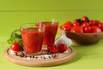Fresh tomato juice in glass mugs. Mugs of tomato juice and fresh tomatoes on a green wooden background.