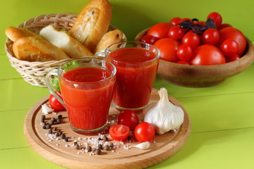 Fresh tomato juice in glass mugs. Mugs of tomato juice, fresh tomatoes and a baguette on a green wooden background.