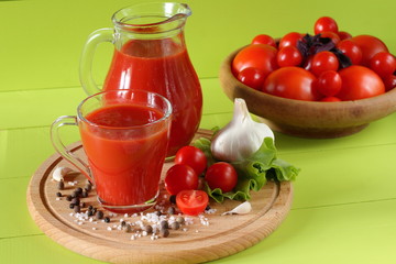 Fresh tomato juice in a glassware. A mug of tomato juice and fresh tomatoes on a green wooden background.