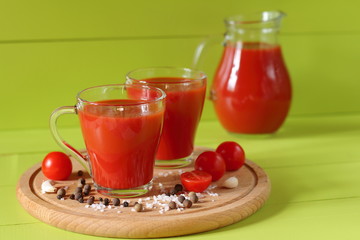 Fresh tomato juice in a glassware. Mugs of tomato juice and fresh tomatoes on a green wooden background.