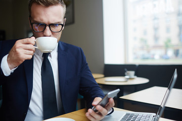 Busy broker texting in smartphone while drinking coffee in cafe