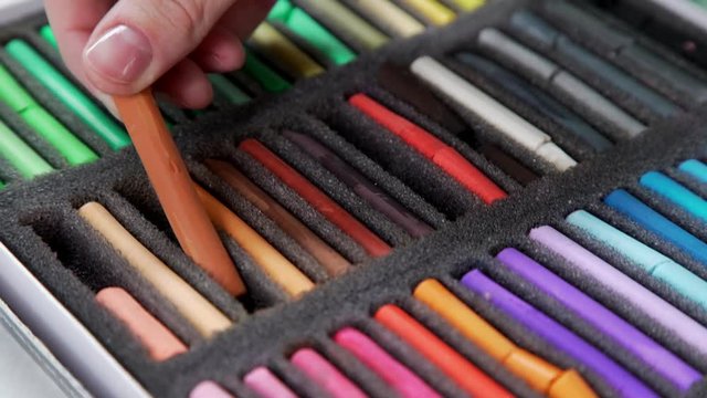 The artist's hands take a brown pastel (soft colored pencils for painting) from a box with a set. Artist's tools for drawing. Painting, creativity. Close-up.