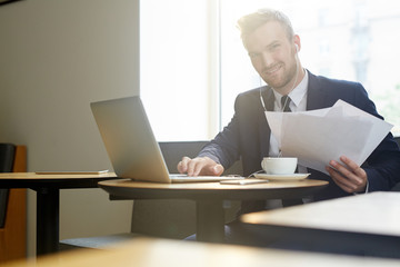 Successful young economist with documents working by cup of tea