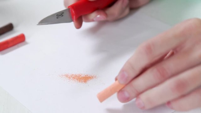 The artist sharpens the red pastel chalk and collects the crumbs to make the shading. The techniques of professional artists: drawing with pastels. Close-up, white background.
