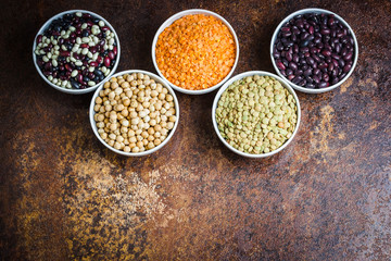 Bowls of various legumes - black, white, red beans, red, green lentils, and chickpeas on old rusty background.
