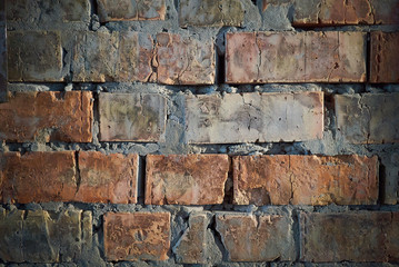 Old red cracked brick wall with rough concrete seams, closeup