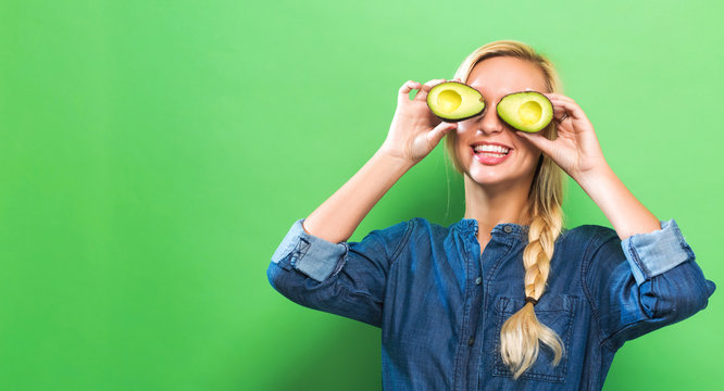 Happy Young Woman Holding Avocado Halves On A Green Background