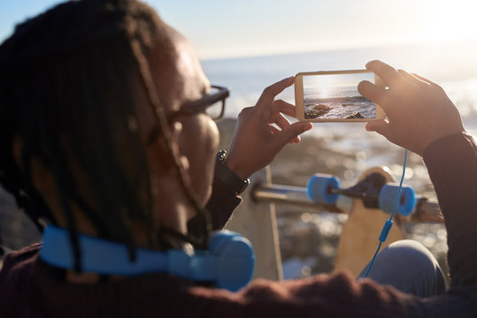Man holding phone taking picture of beautiful seaside ocean scen