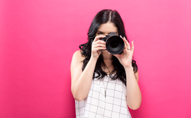  Young woman holding a camera on a pink background