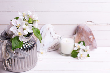 Apple tree flowers in vase,  decorative heart and candles on white wooden background.