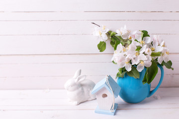  Apple tree flowers in pitcher, Easter rabbit and  decorative bird house on white wooden background.