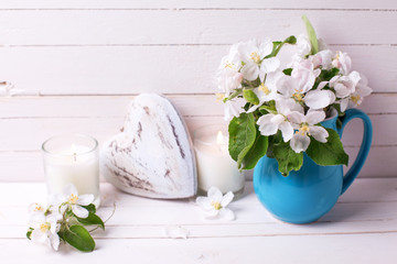 Apple tree flowers,  decorative heart and candles on white wooden background.