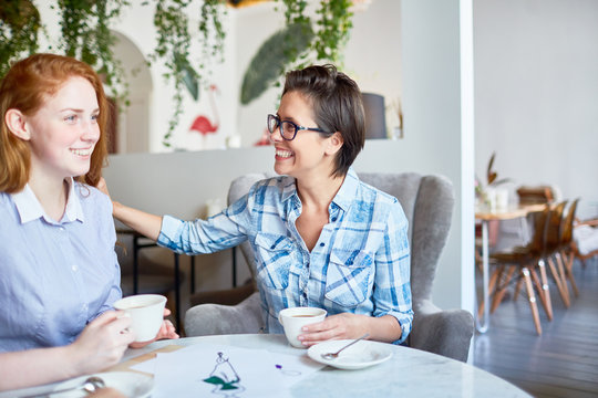 Happy employer lauding happy young subordinate by cup of coffee in cafe