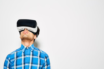 Concentrated young man looking upwards while playing game with help of VR headset, studio shot