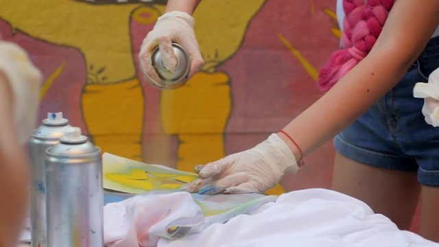 cans of Colorful paint in hand close-up, painting clothes with spray paint outdoors, design clothes of handmade on open air, colored t-shirts Painted in street style, street art,