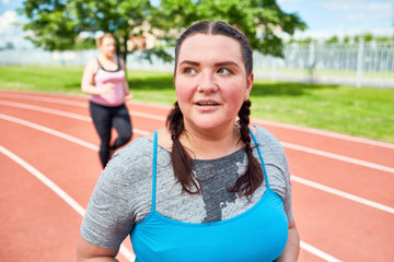 Plump woman in activewear sweating on stadium during workout