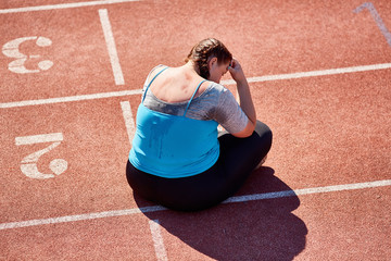Unlucky woman sitting on stadium racetrack after hard workout