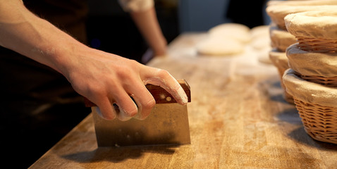 baker portioning dough with bench cutter at bakery - obrazy, fototapety, plakaty