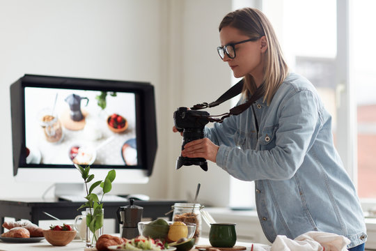 Profile view of concentrated young food photographer taking picture of served table for healthy breakfast, spacious production studio on background