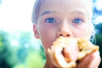 Little child girl eating a hot dog outdoors in summer