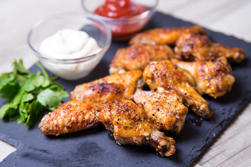 Chicken wings of a barbecue with two sauces on a black board. Close-up. Selective focus.