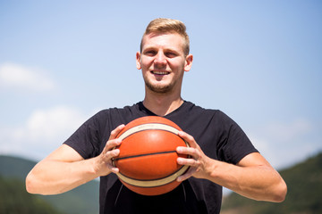 Handsome tall blonde person holding a ball and looking at the court smiling, blue sky background