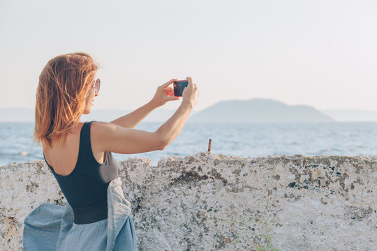Young woman taking a photo using smartphone by the seaside