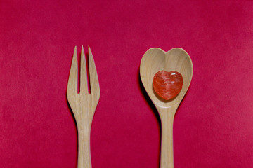 Heart-shape toffee on wooden spoon and fork isolated on red background