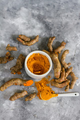 Turmeric root and ground turmeric. White bowl, gray background.