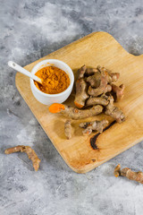 Turmeric root and ground turmeric. White bowl, gray background. 