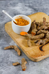 Turmeric root and ground turmeric. White bowl, gray background. 