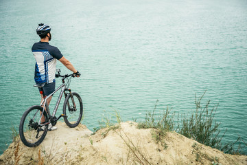 man with bicycle stand on the hill and looking at the lake