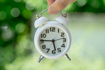 hand holding white alarm clock as business or time countdown concept with green bokeh background