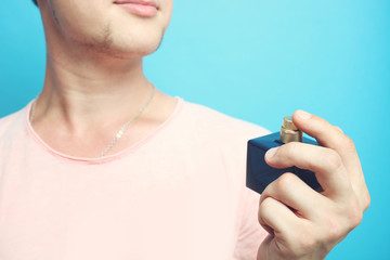 Fototapeta premium The guy holds a bottle of perfume on a blue background in his hand.