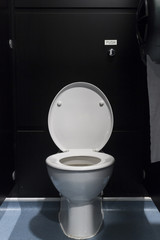 White porcelain toilet with lid up in a black stall
