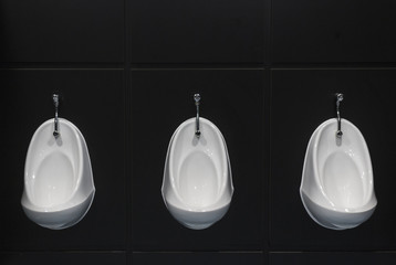 3 urinals in a row on a black wall