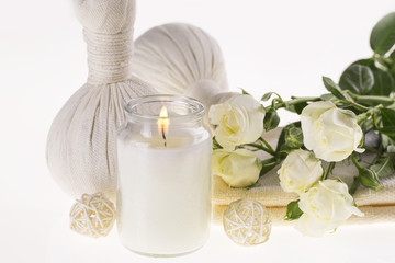 Fototapeta na wymiar Spa. Burning candle, herbal balls for massage, white roses and a towel on a white background