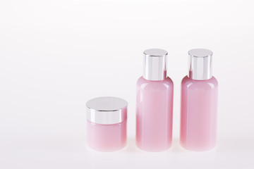 Two bottles and one jar with a cosmetic pink color on a white background.