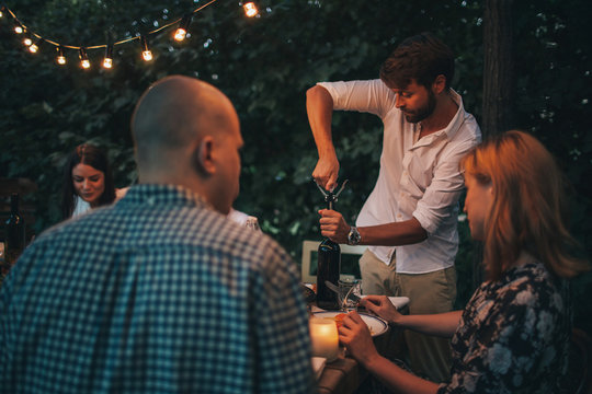 Group of friends enjoying together at a dinner party. A man opening a bottle of wine