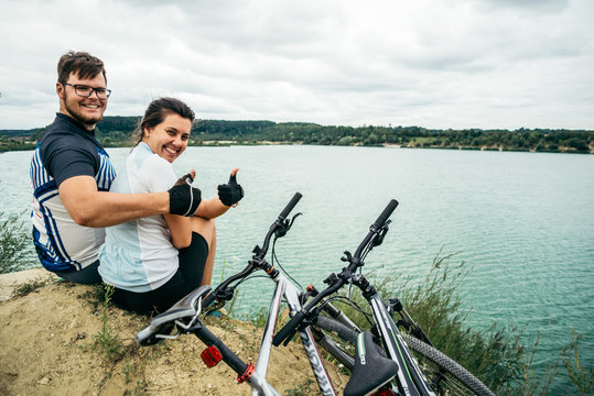 cuple of sportmen sitting near lake with bicycles