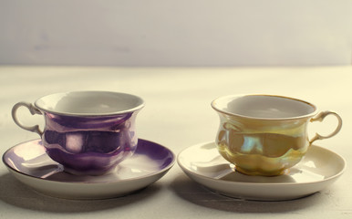 Empty colorful porcelain tableware. Yellow and violet cups on lilac background. Toned