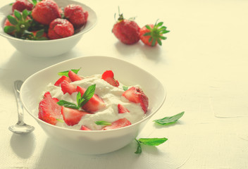 Breakfast with bowl of thick organic greek yogurt and fresh strawberries on white backgfound. Toned