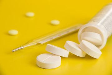 Round tablets and a mercury thermometer on a yellow background © Sklyarov