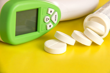 Round tablets and infrared thermometer on a yellow background © Sklyarov