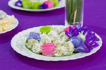 traditional thai desserts , Colorful of Thai steamed layer cake in cube and rose shape,call Khanom Chan in Thai copy space on the purple table